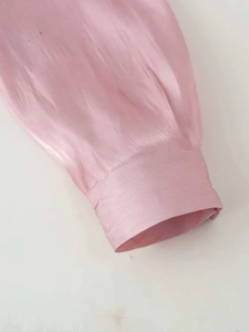 Close-up of pink satin shirt sleeve with refined stitching and glossy fabric detail