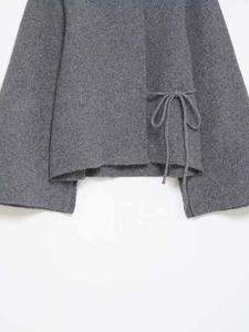 Detailed close-up of grey knit cardigan featuring side tie-up bow and textured wool fabric