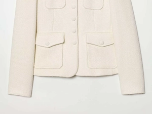 Detailed view of cream-colored tweed jacket featuring four flap pockets and textured fabric