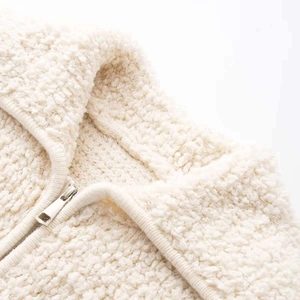 Detailed macro view of cream boucle knit fabric texture and high-quality silver metal zipper