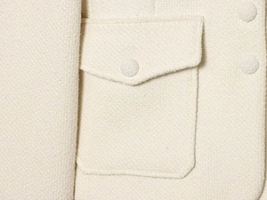 Close-up of cream tweed jacket pocket with textured woven fabric and fabric-covered button