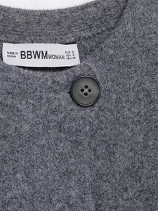 Macro detail of grey knitted cardigan texture featuring a matte black button and brand label