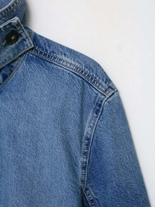 Detail of blue denim jacket with yellow stitching and brown button on collar