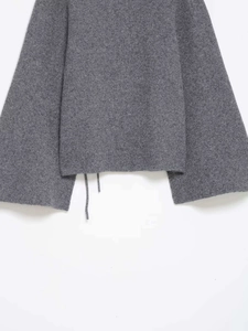 Detail view of a grey knit cardigan featuring loose dropped shoulders and hem tie details