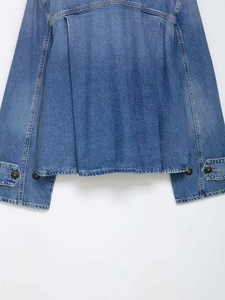 Detail of blue denim jacket back featuring deep box pleat and buttons on the cuffs
