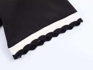 Detail of black polo shirt sleeve featuring white stripes and scalloped edge knit texture
