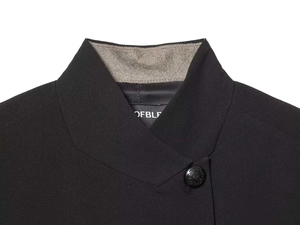 Macro detail of asymmetric blazer collar featuring gray quilted lining and relief button