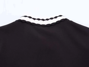 Close-up of black polo top showing scalloped edges and black and white striped collar detail