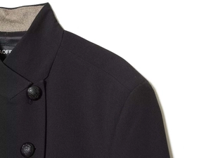 Macro detail of the mandarin collar jacket featuring embossed shield buttons and wool trim