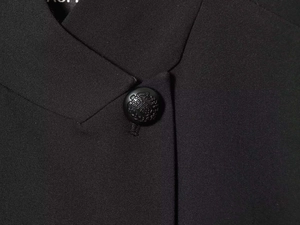 Detail of minimalist black blazer showing structured lapel and embossed crest button