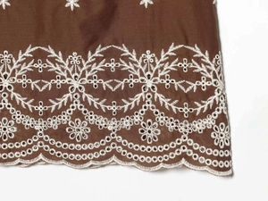 Detail von kaffeebraunem Stoff mit weißer Blumenstickerei und gewelltem Saum