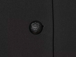 Detail of elegant black blazer featuring a resin button with embossed crest and crown