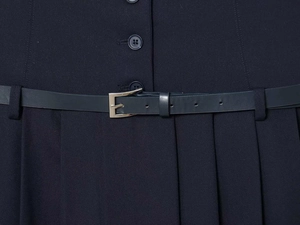 Detailed macro view of black pleated dress featuring a slim waist belt and button closures