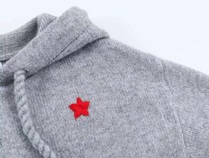 Detailansicht eines grauen Strick-Hoodies mit rotem Sternstick und Kordelzugband