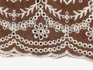 Detailaufnahme von braunem Stoff mit weißer Broderie Anglaise Stickerei und Wellensaum