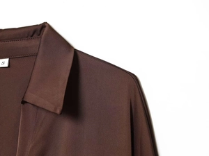 Detail view of the brown satin shirt collar and S size label with smooth fabric texture