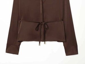Detail of dark brown satin shirt featuring a drawstring waist with gold metal tips