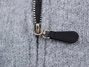 Detail von Silberreißverschluss und schwarzem Lederzug an grauer Jacquard-Strickjacke