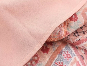 Close-up of pink chiffon fabric with paisley print and precise sewing details on the dress