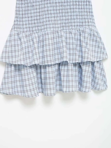 Detail view of light blue plaid dress showing tiered ruffles and smocked fabric texture