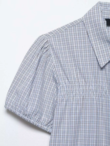 Détail de chemisier à carreaux bleus et blancs avec smocks et manches bouffantes