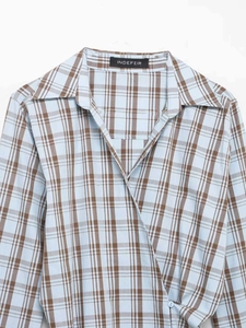 Detail eines blau-braun karierten Wickelshirts mit V-Ausschnitt und weißem Knopfverschluss
