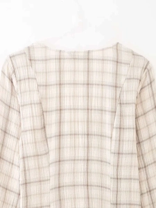 Détail de la texture du tissu à carreaux beige et de la couture du col d'une robe en V
