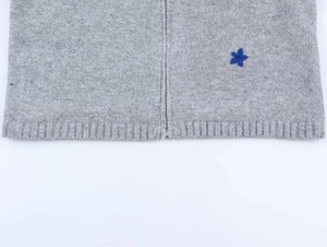 Detailansicht der grauen Strickjacke mit Reißverschluss und Sternenstickerei am Saum