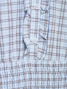 Detail of blue plaid fabric showing smocking texture, ruffles, and white buttons
