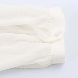 Detailed close-up of cream pleated shirt sleeve with matching fabric-covered button