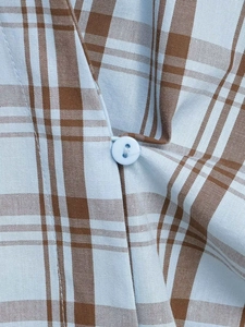 Makro-Detail von blau-braunem Karo-Stoff mit einem runden Vierloch-Knopf am Hemd