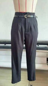 Detail of high-waisted black trousers featuring fine pleats and a matching slim leather belt