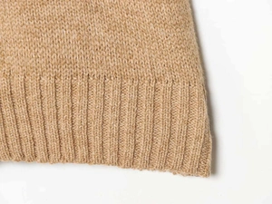 Macro detail of camel wool knit short sleeve vest showing ribbed hem and soft fiber texture