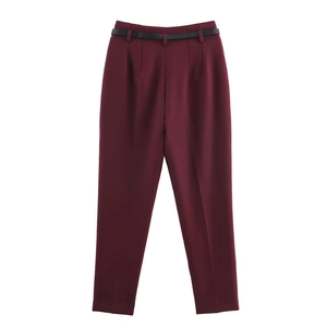 Close-up of wine red high-waisted trousers with pleats and a slim black belt detail