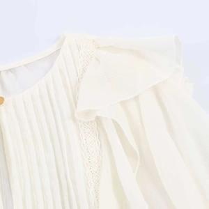 Detail view of white chiffon blouse showing pleat texture and ruffled lace edges