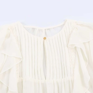 Detail of white ruffled chiffon blouse with lace inserts and gold button back closure