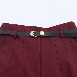 Detail of burgundy high-waisted trousers with black leather belt and gold buckle