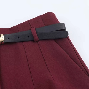 Detail of high-waisted burgundy trousers featuring pleated waist and thin black belt