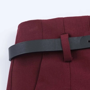 Close-up of burgundy high-waist trousers featuring a black leather belt and side pocket detail