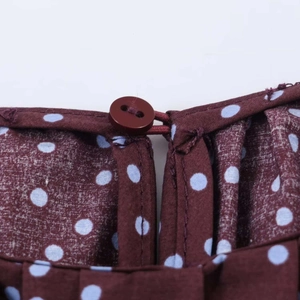 Detalle del cuello con abertura de lágrima y cierre de botón en blusa de lunares