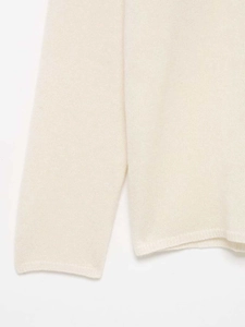 Vue macro de la maille blanc crème et des détails en dentelle sur l'ourlet de manche