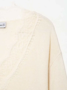Gros plan d'un pull en maille crème avec dentelle au col et étiquettes de taille