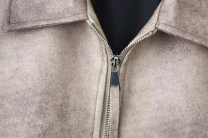 Dettaglio del colletto a revers e della zip metallica sulla giacca scamosciata beige