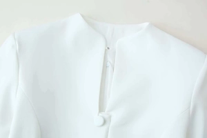 Detailed view of white standing collar with fabric-covered buttons and hidden zipper