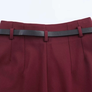 Detail view of burgundy trousers waistline featuring woven texture and a slim black leather belt