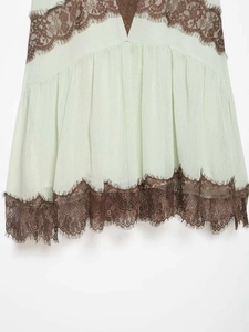 Close-up of light green dress with dark brown lace trim and pleated texture detail