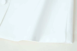 Detail of the white fabric texture and button on the waist of a minimalist summer dress
