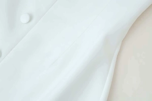 Close-up of a fabric-covered button and seam details on a white structured dress