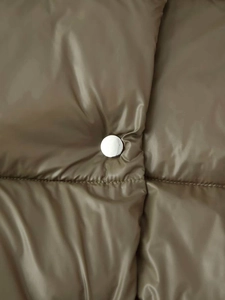 Close-up of olive green puffer jacket featuring horizontal quilting and a silver metal button