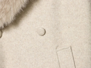 Détail du manteau en laine avec col en fourrure, bouton gainé et couture de poche